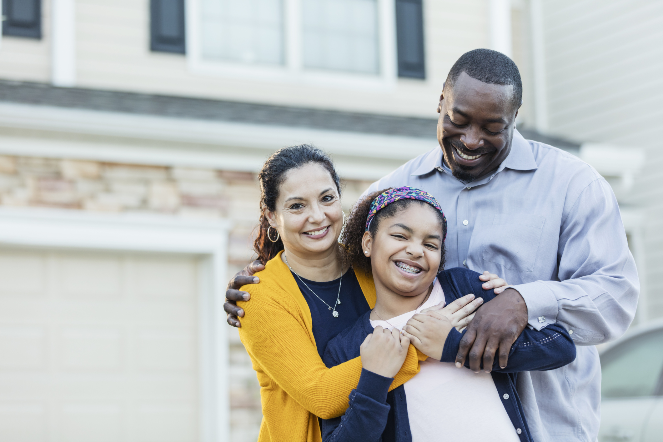 Family smiling together in front of a house, embracing warmly.