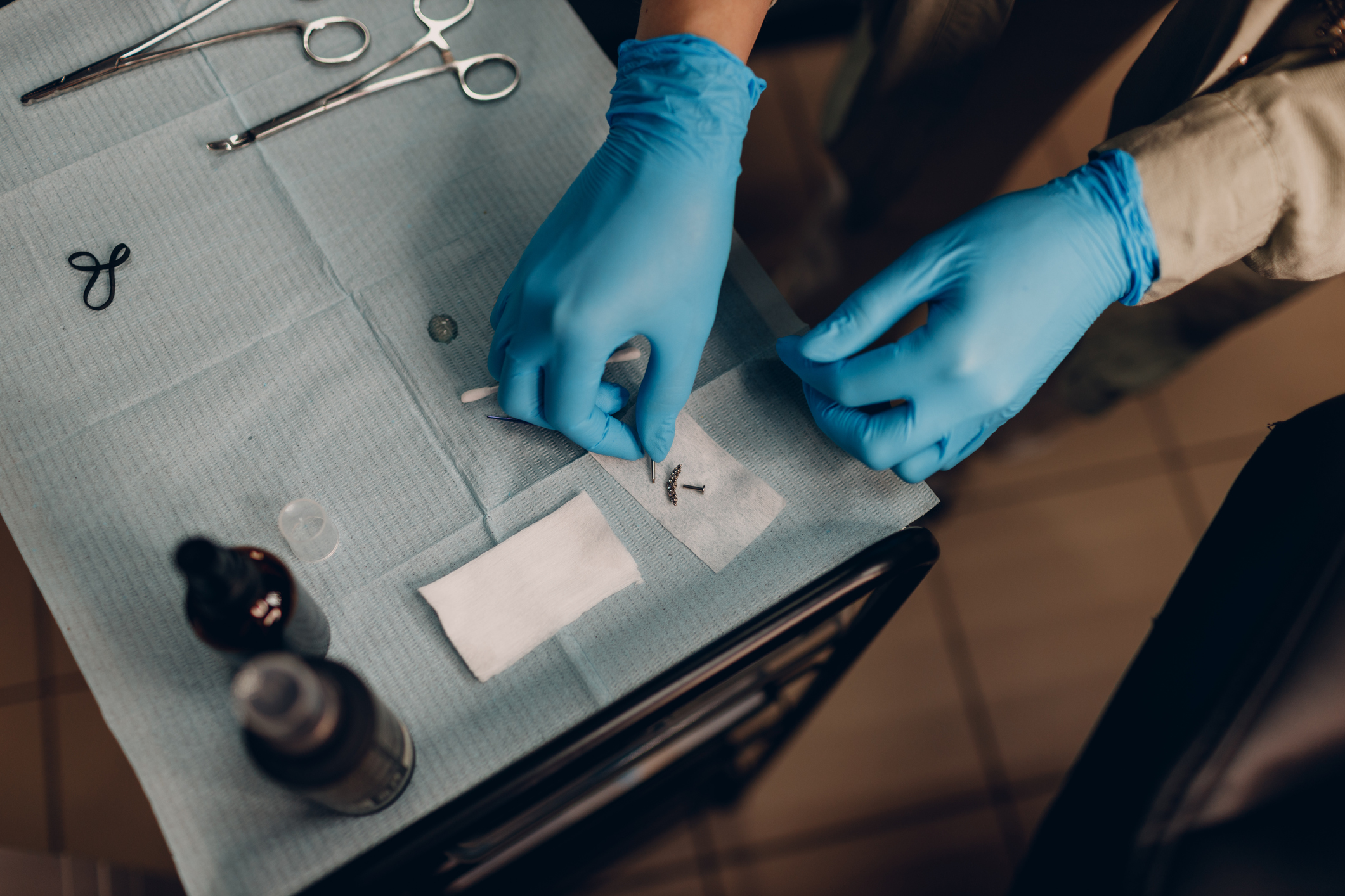 Hands wearing blue gloves arrange tools on a medical tray.