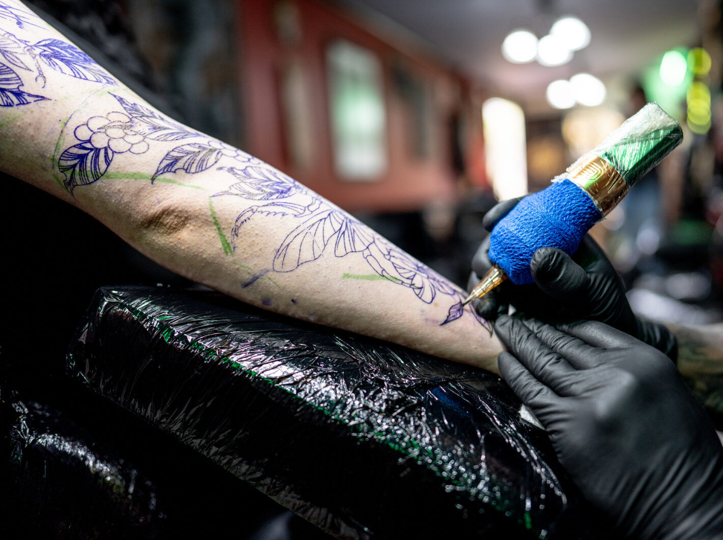 Tattoo artist working on floral design on arm with gloved hands