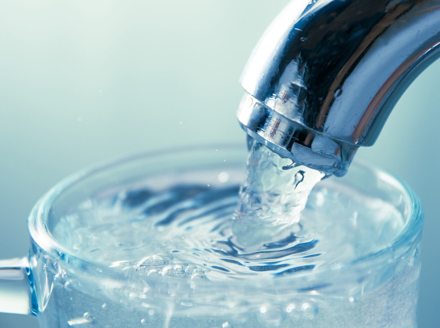 Water pouring from a chrome faucet into a clear glass