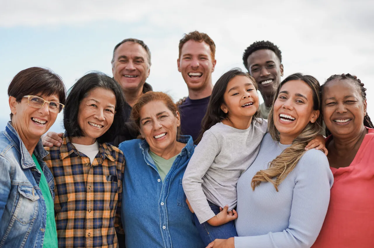 Group of diverse people smiling outdoors, displaying happiness and togetherness.