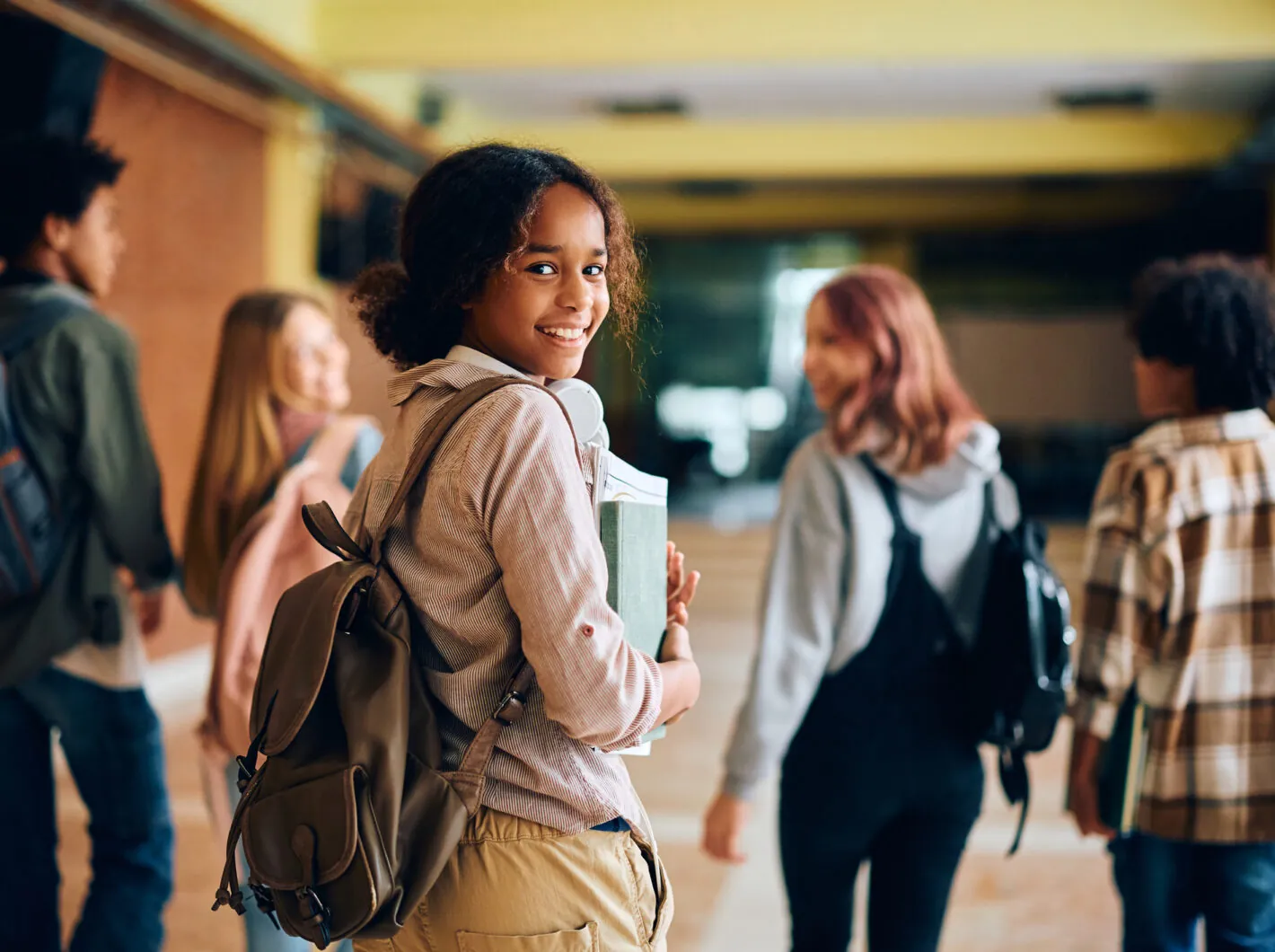 Group of smiling students walking through a school hallway, one looking back.