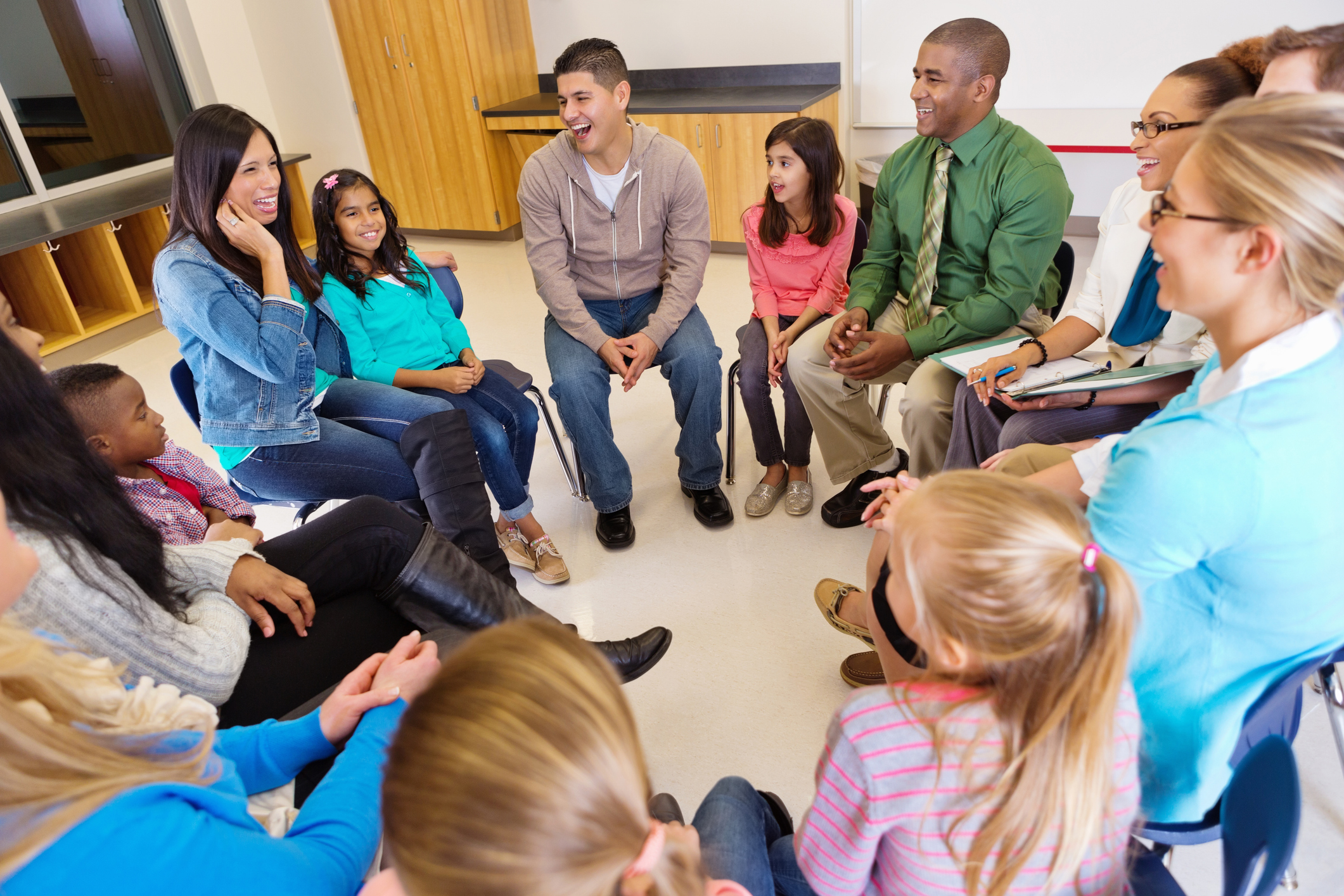 A group of adults and children sit in a circle having a conversation.