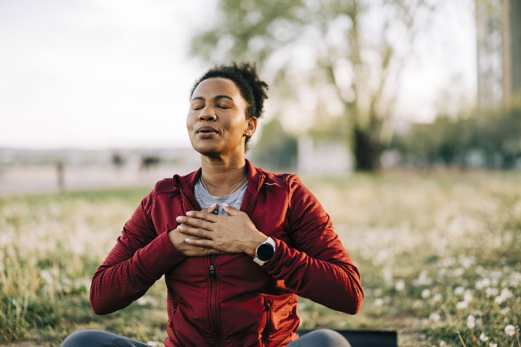 Person sitting outdoors in meditation, hands on chest.