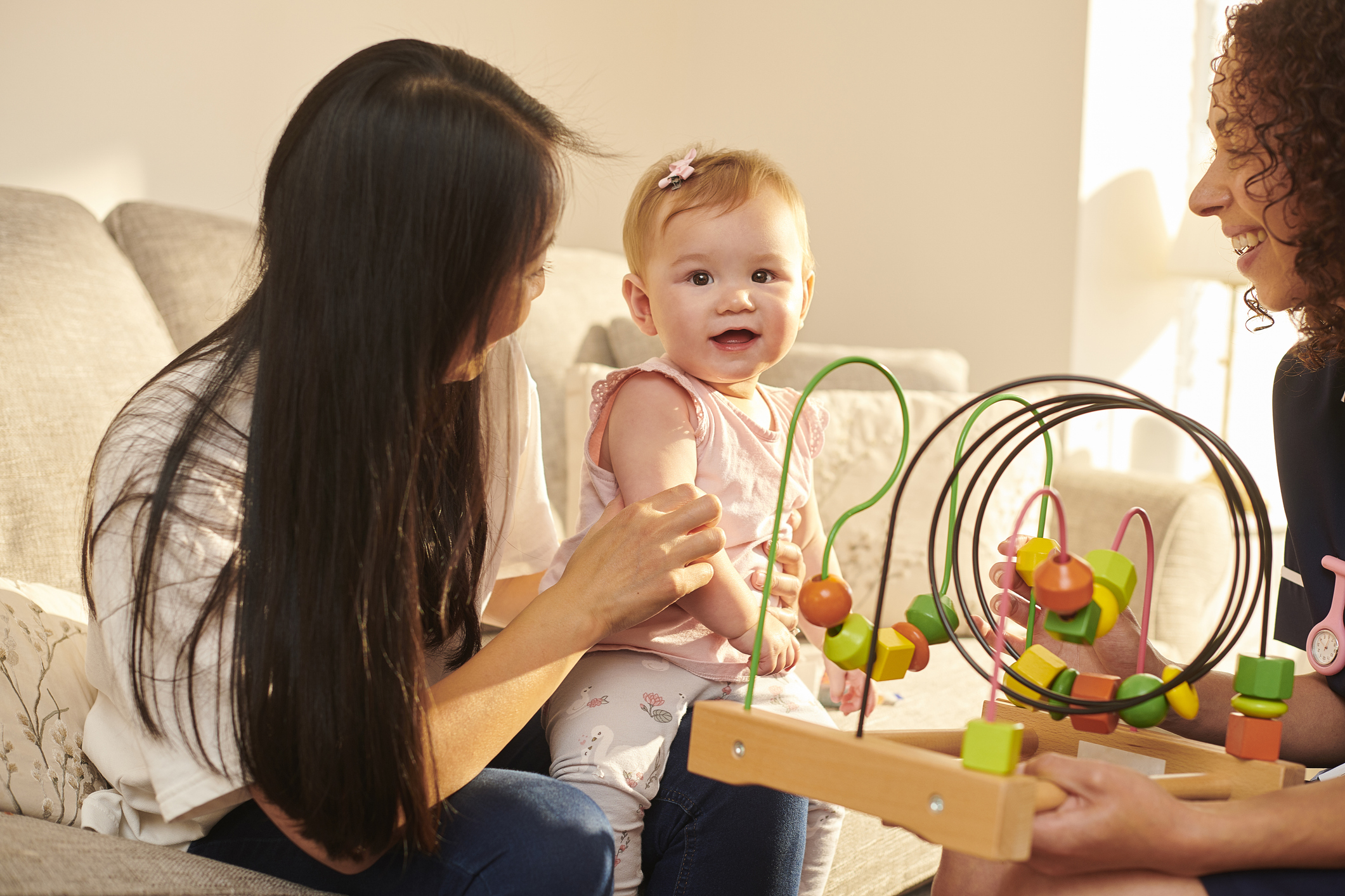 Baby smiling between two adults with colorful wire bead toy.