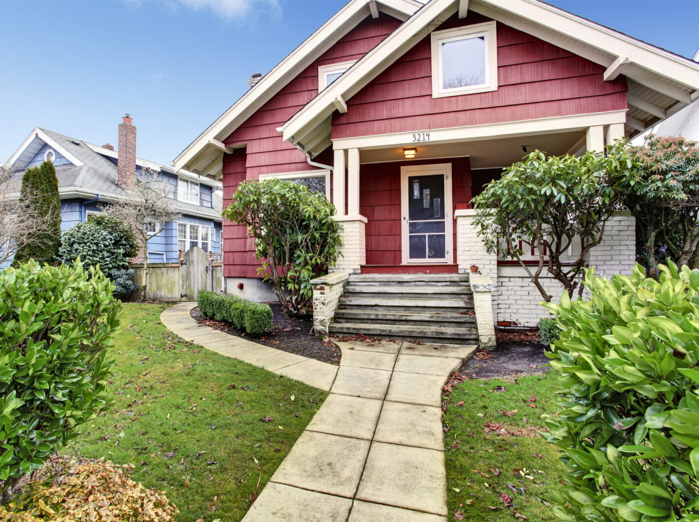 Red house with old brick steps, front yard, and green shrubs. House number 3214 displayed above the door.