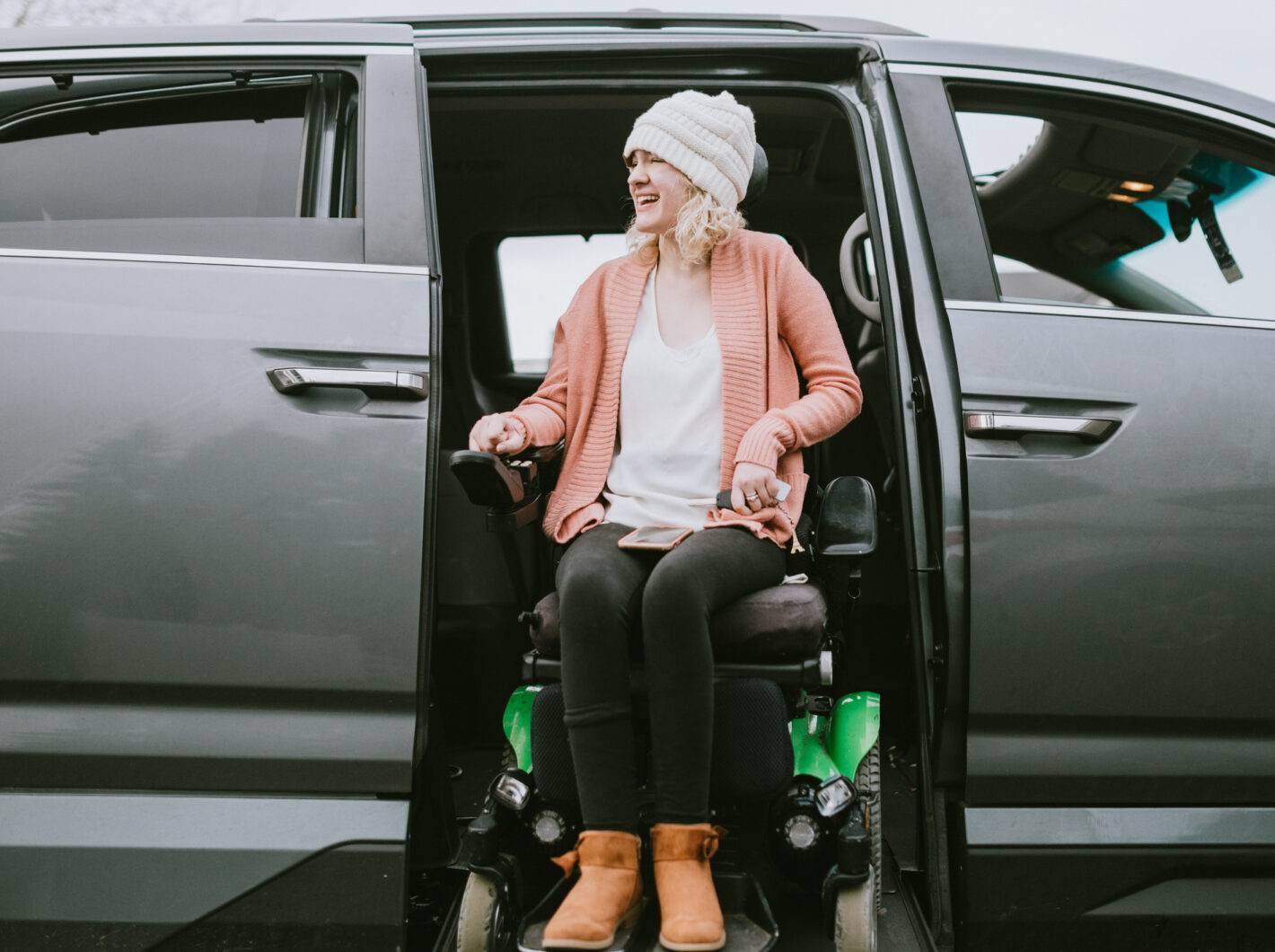 Photo of a woman in a wheelchair being lifted down out of a vehicle