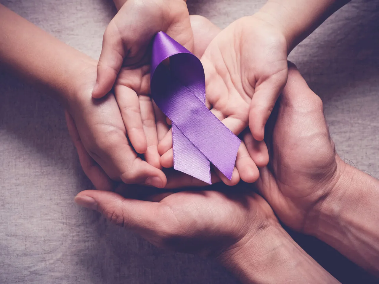 Hands holding a purple ribbon symbolizing support or awareness.