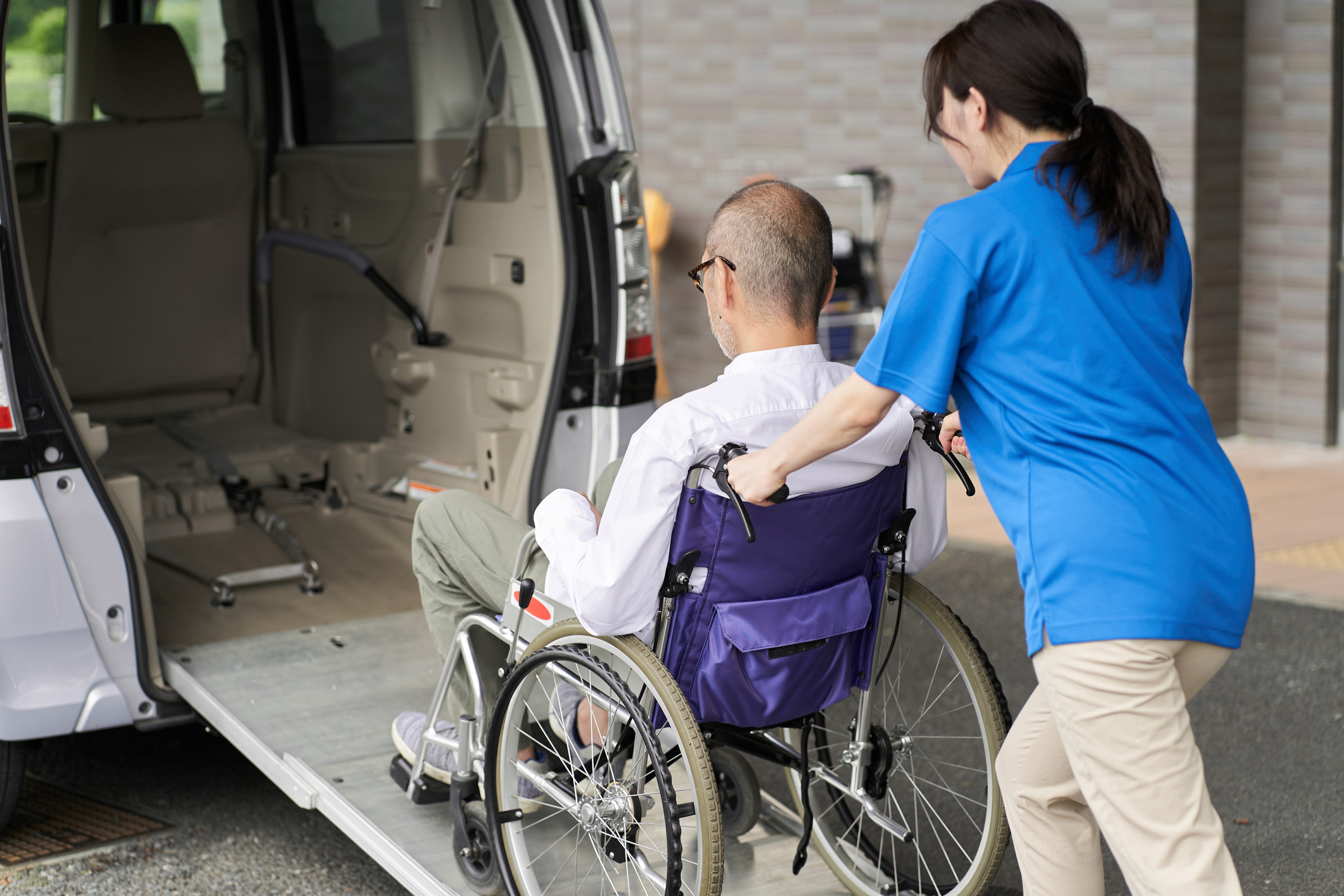 Person in blue shirt assists wheelchair user into van ramp