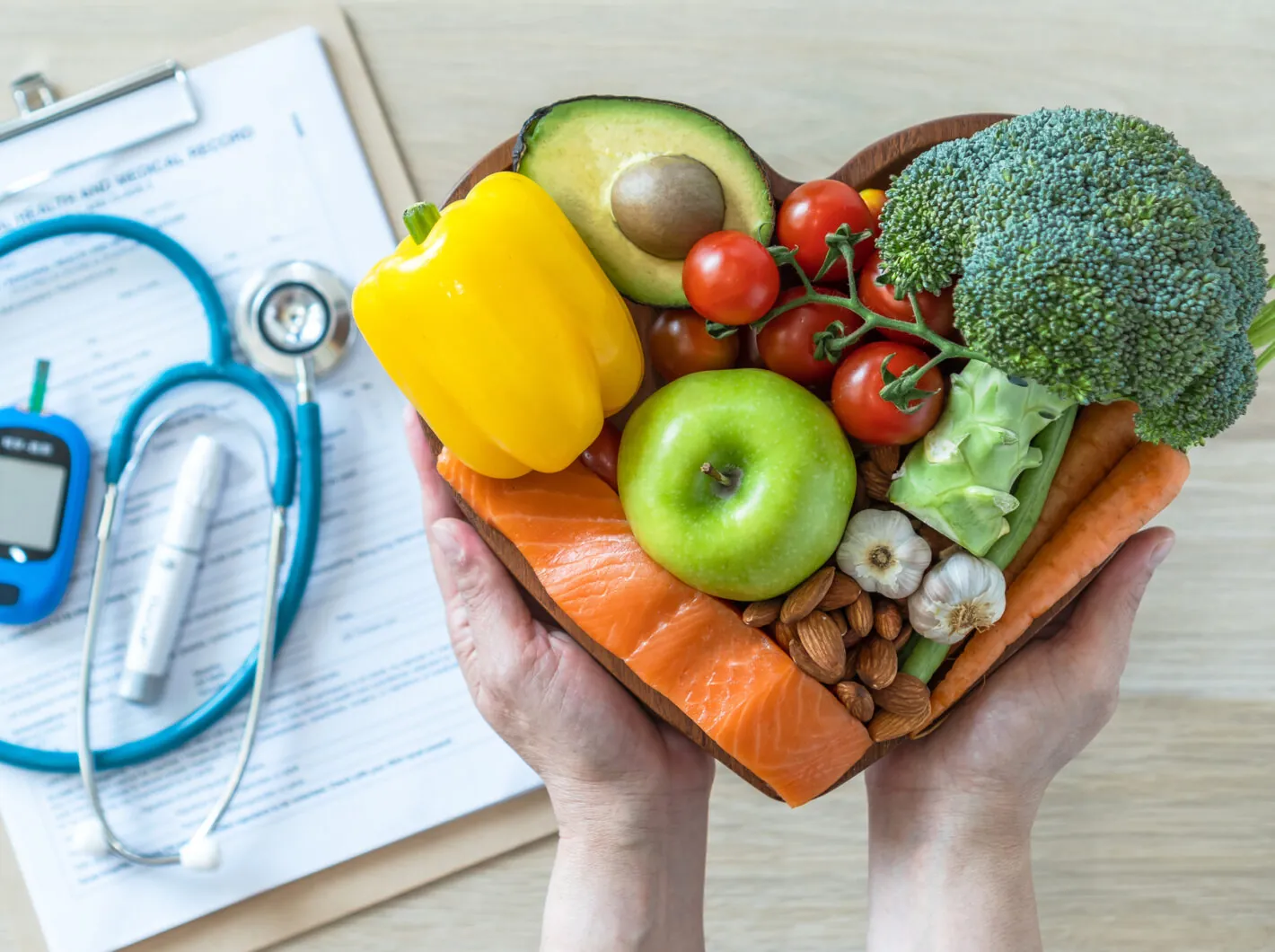 Photo of hands holding a bowl of fruits and veggies in front of a clipboard and blood sugar monitor