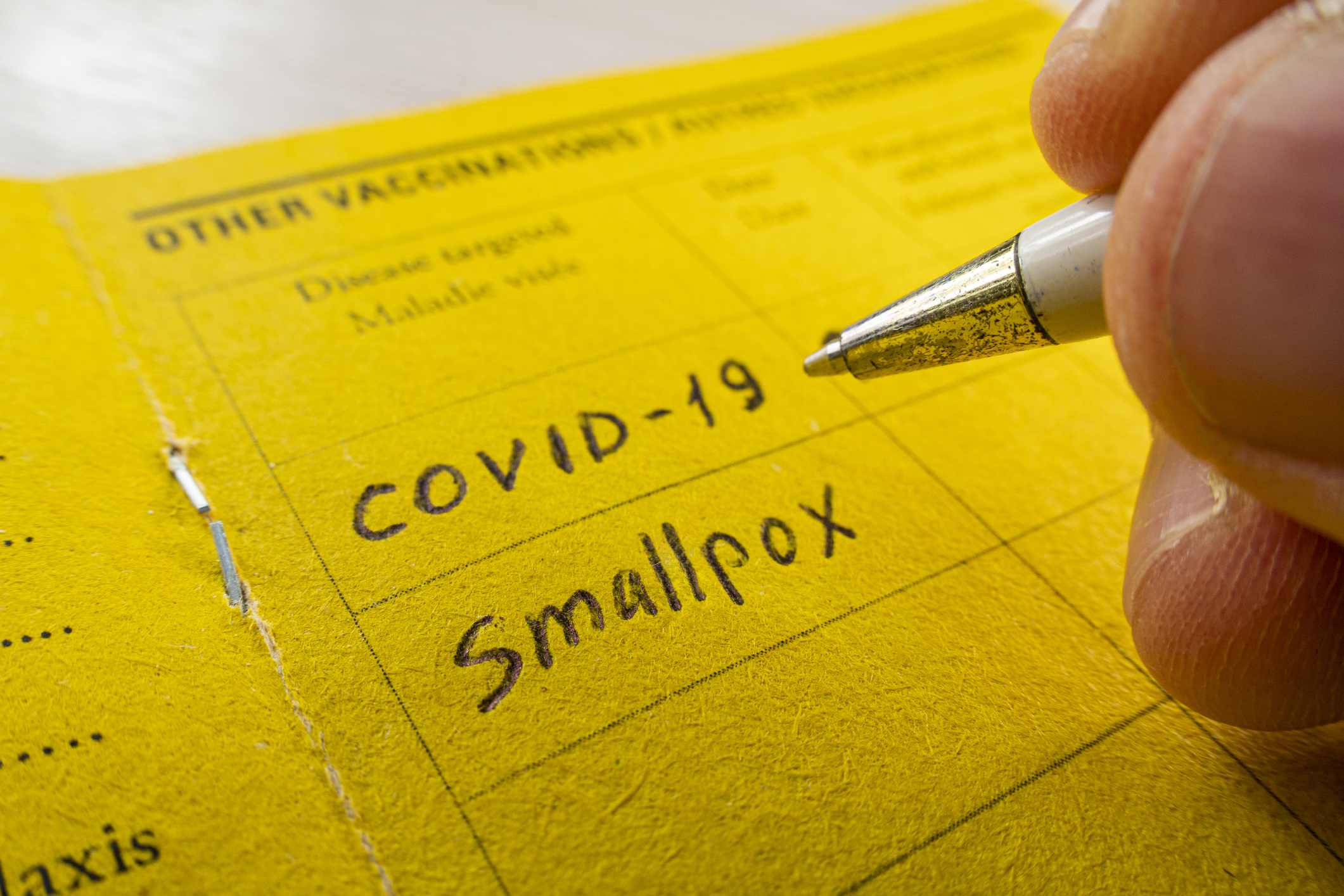 Photo of handwriting "COVID-19" and "Smallpox" on yellow vaccination card with pen.