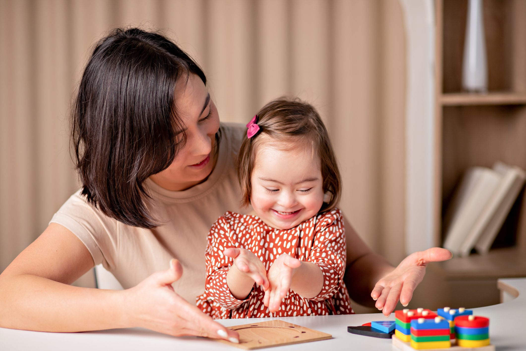 Photo of a woman and child with Down syndrome playing, smiling, in educational activity.