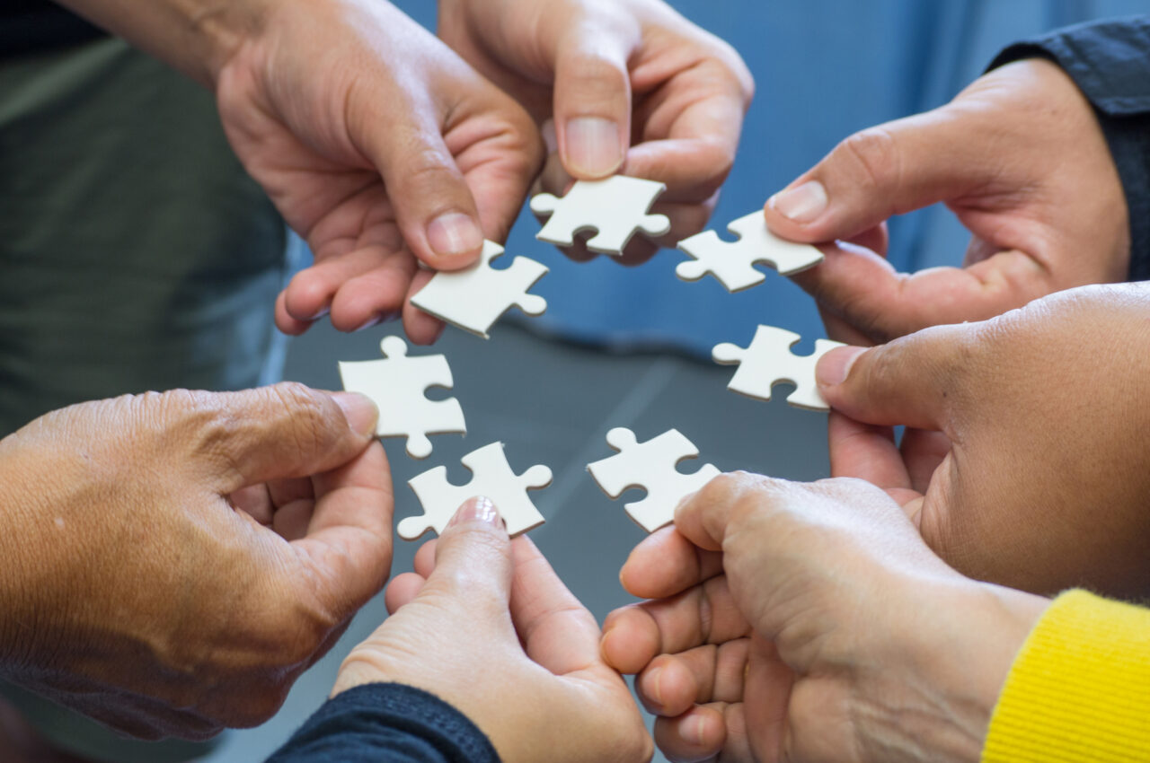 Hands holding white puzzle pieces, forming a circle, symbolizing collaboration.
