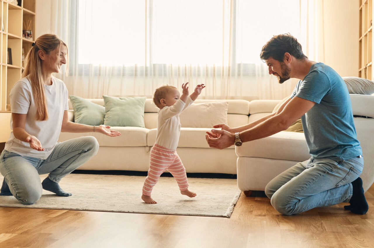 Photo of parents helping their baby take the first steps