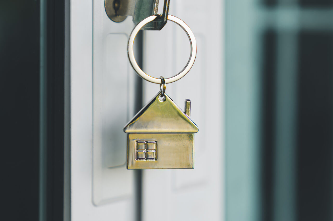 House-shaped keychain hanging from a key in a door.