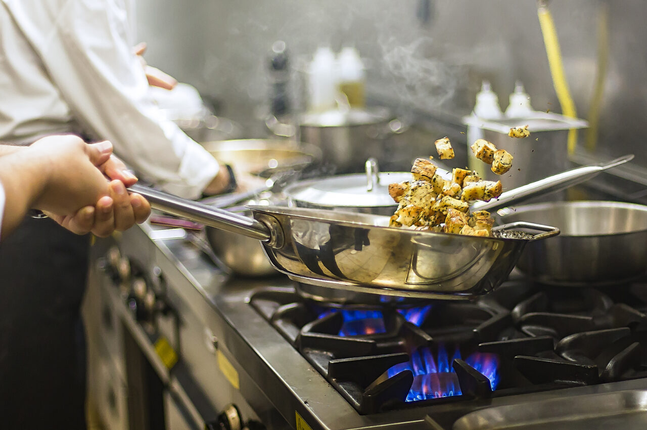 Photo showing a chef tossing vegetables in a pan over a gas stove fire