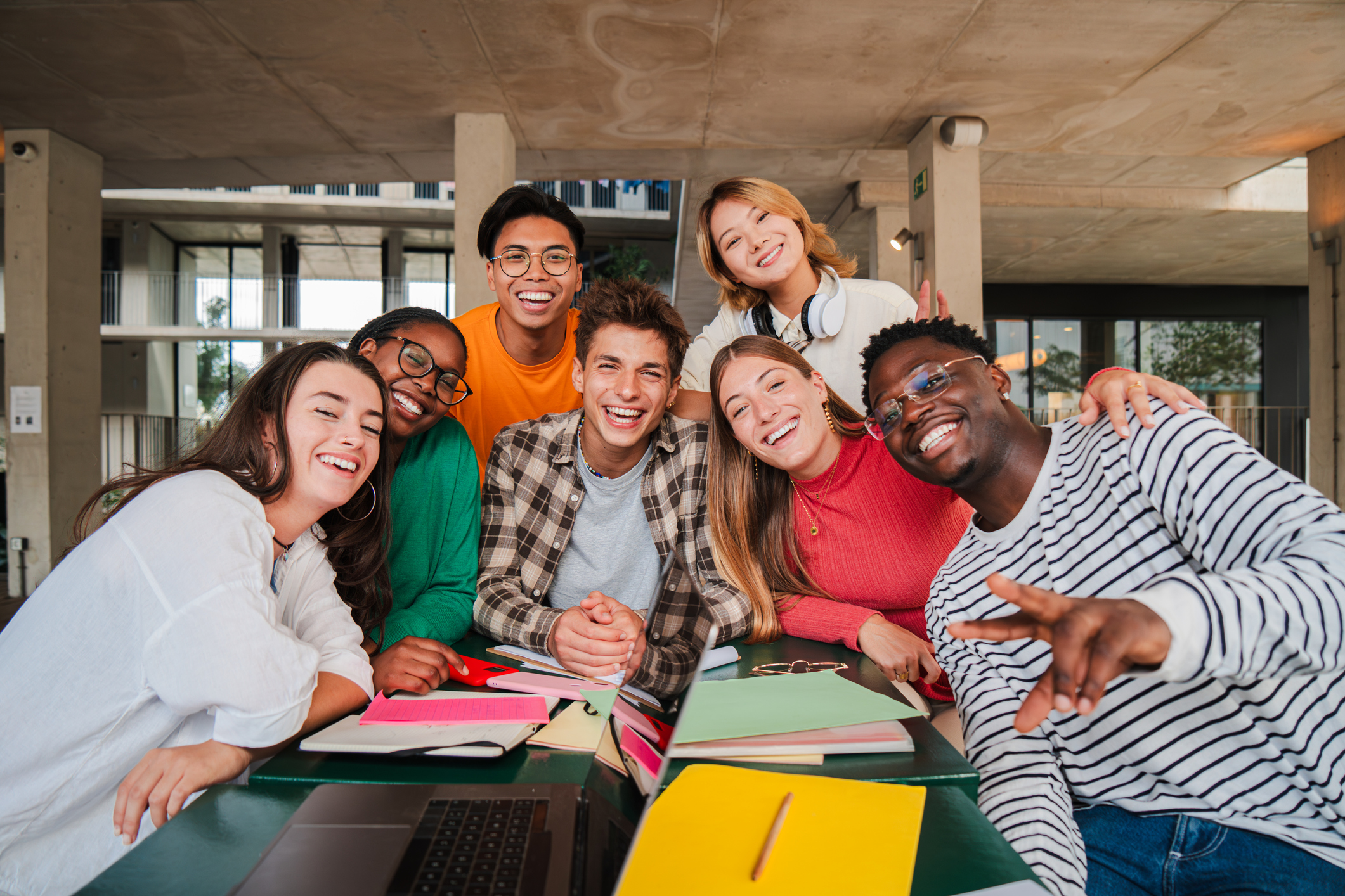 Diverse group of seven young adults smiling around a table with notebooks and a laptop.