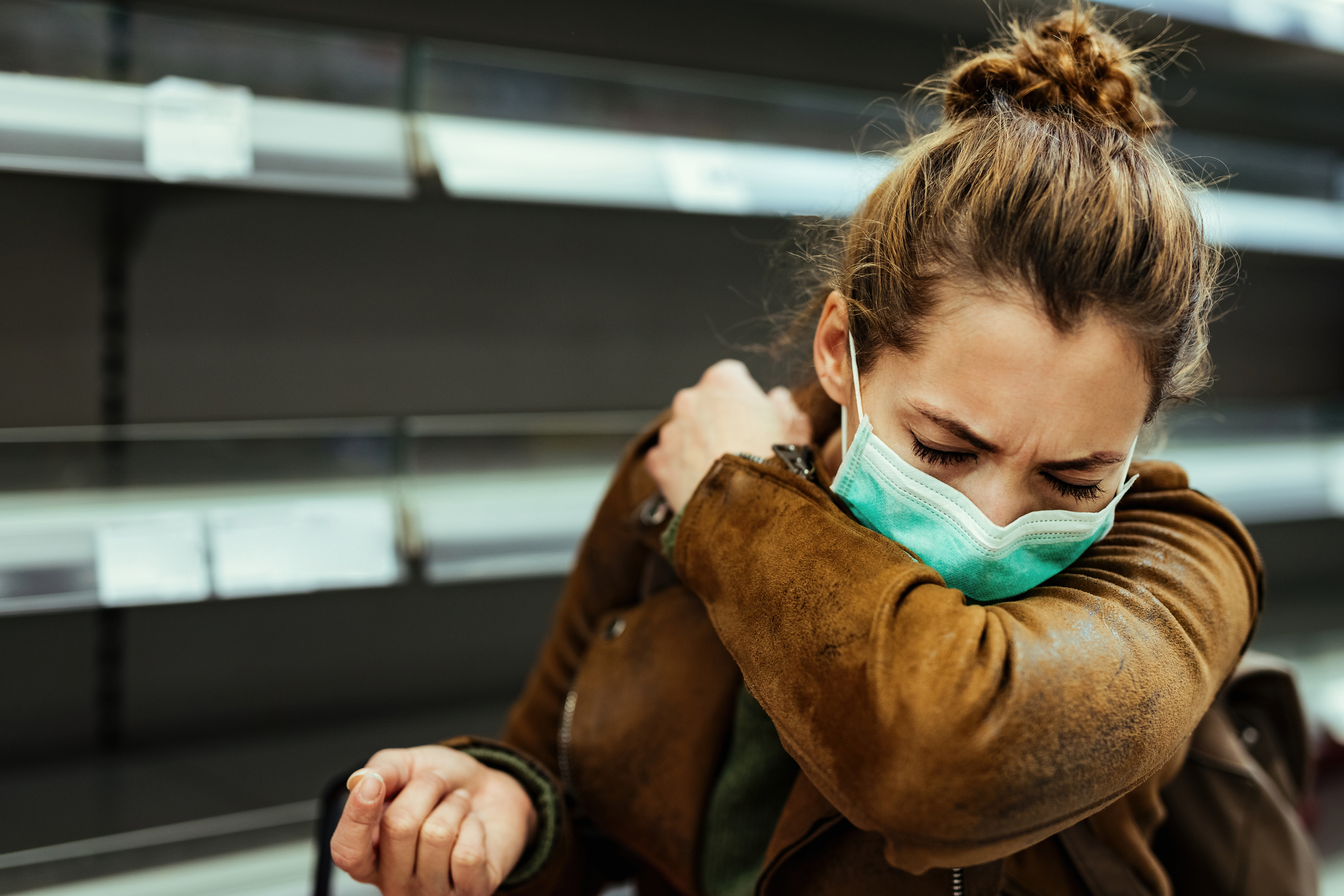 Woman wearing a mask, sneezing into elbow in a store.