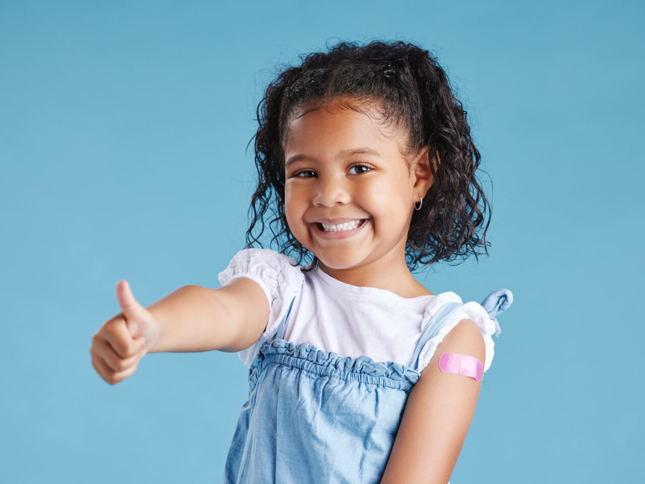 Smiling child gives a thumbs up, wearing a pink bandage on arm