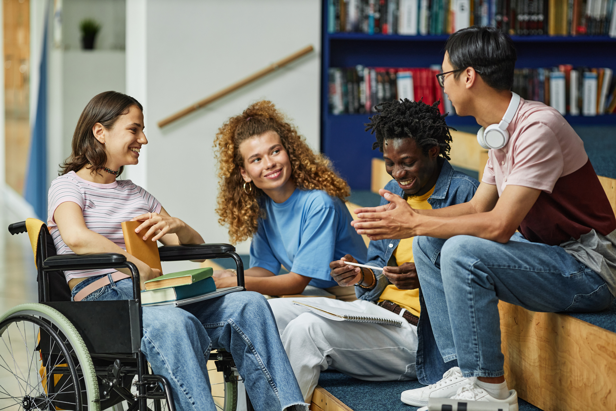 Diverse group of students engaging in discussion, smiling, and sitting indoors with books and notepads