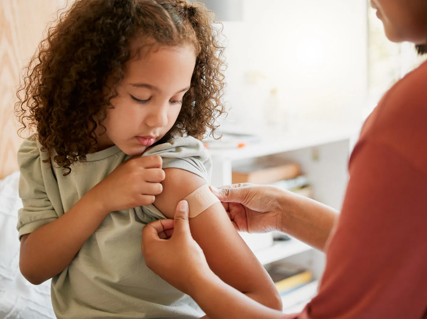 Child receiving a band-aid on arm after vaccination, looking down