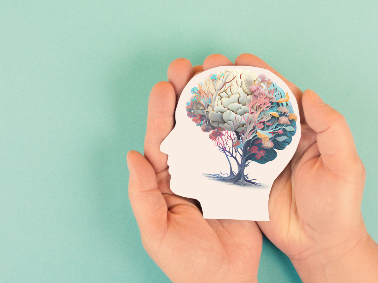 Hands holding paper cutout of head with brain as a colorful tree