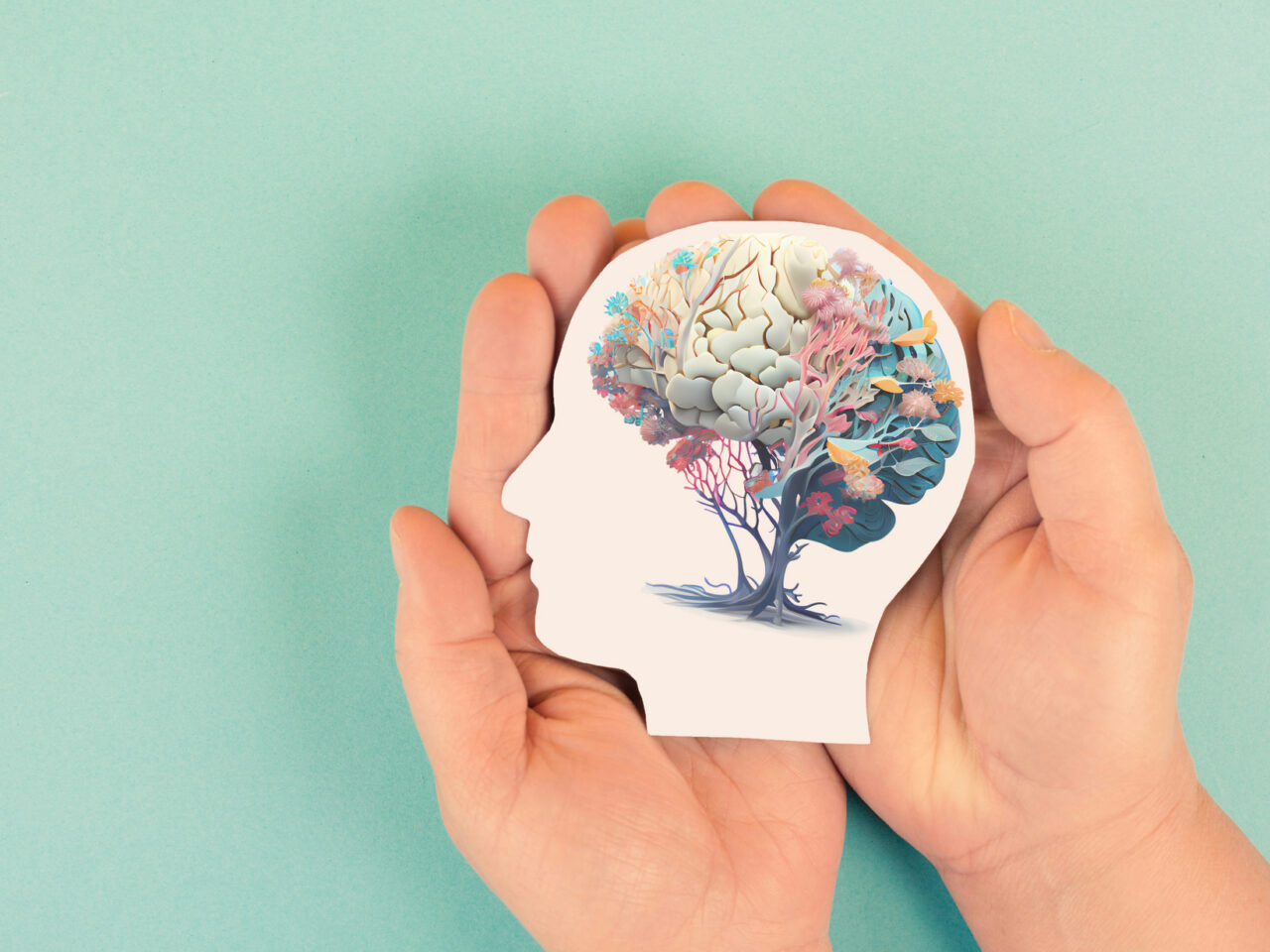 Hands holding paper cutout of head with brain as a colorful tree