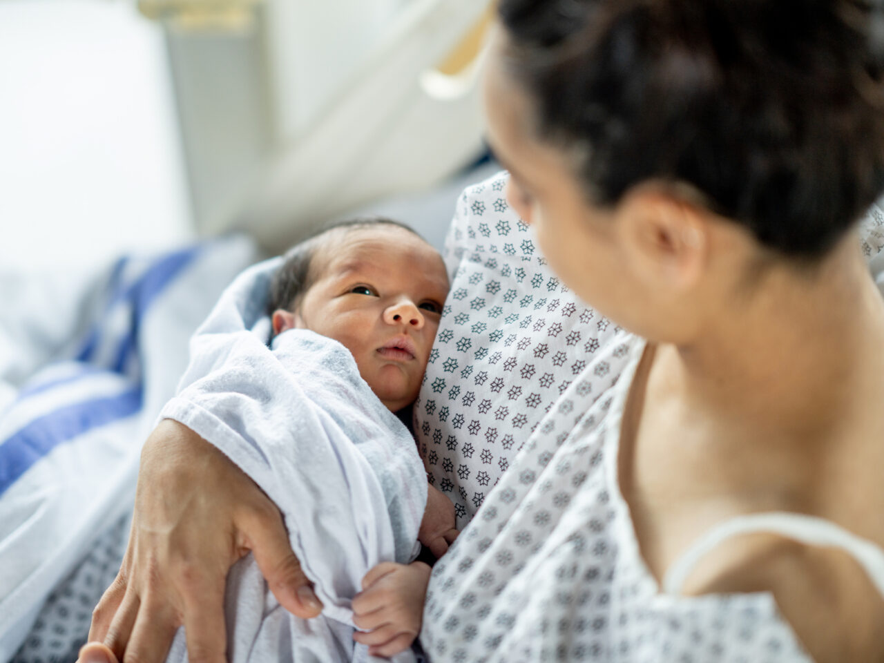 Mother gently cradling newborn wrapped in a white blanket, both gazing at each other warmly
