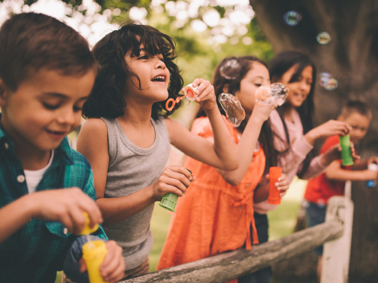 Children joyfully blowing bubbles outdoors near a wooden fence
