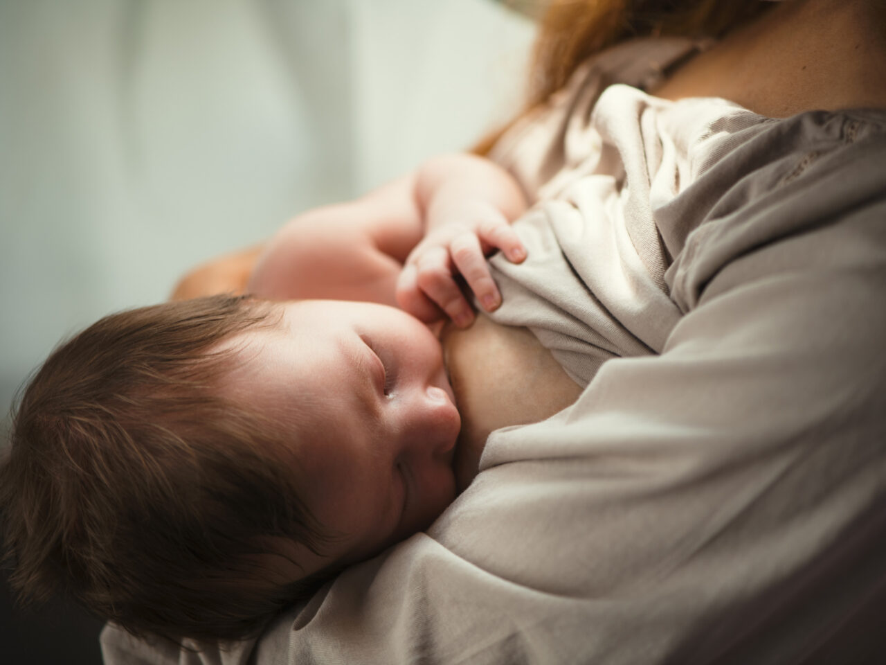 Baby breastfeeding, nestled in parent's arms, serene setting