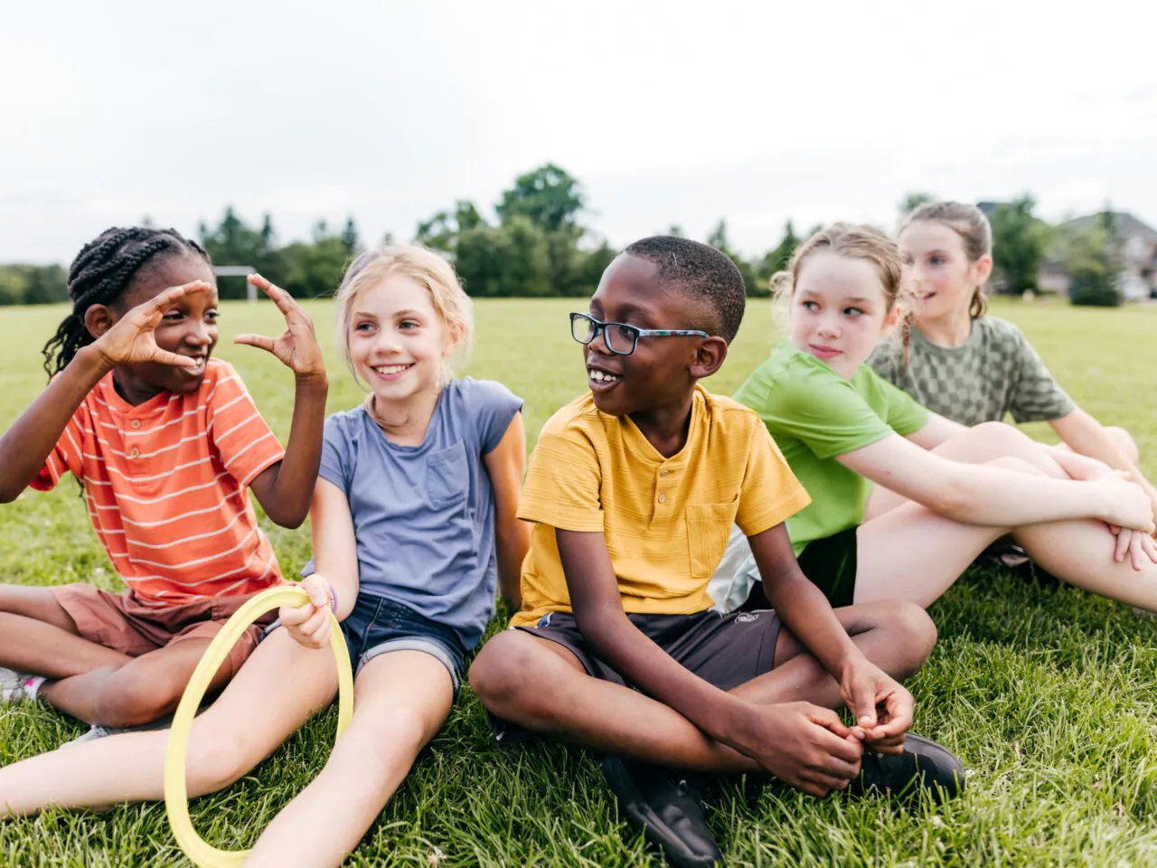 Children sitting on grass, smiling and talking, one holding a hoop